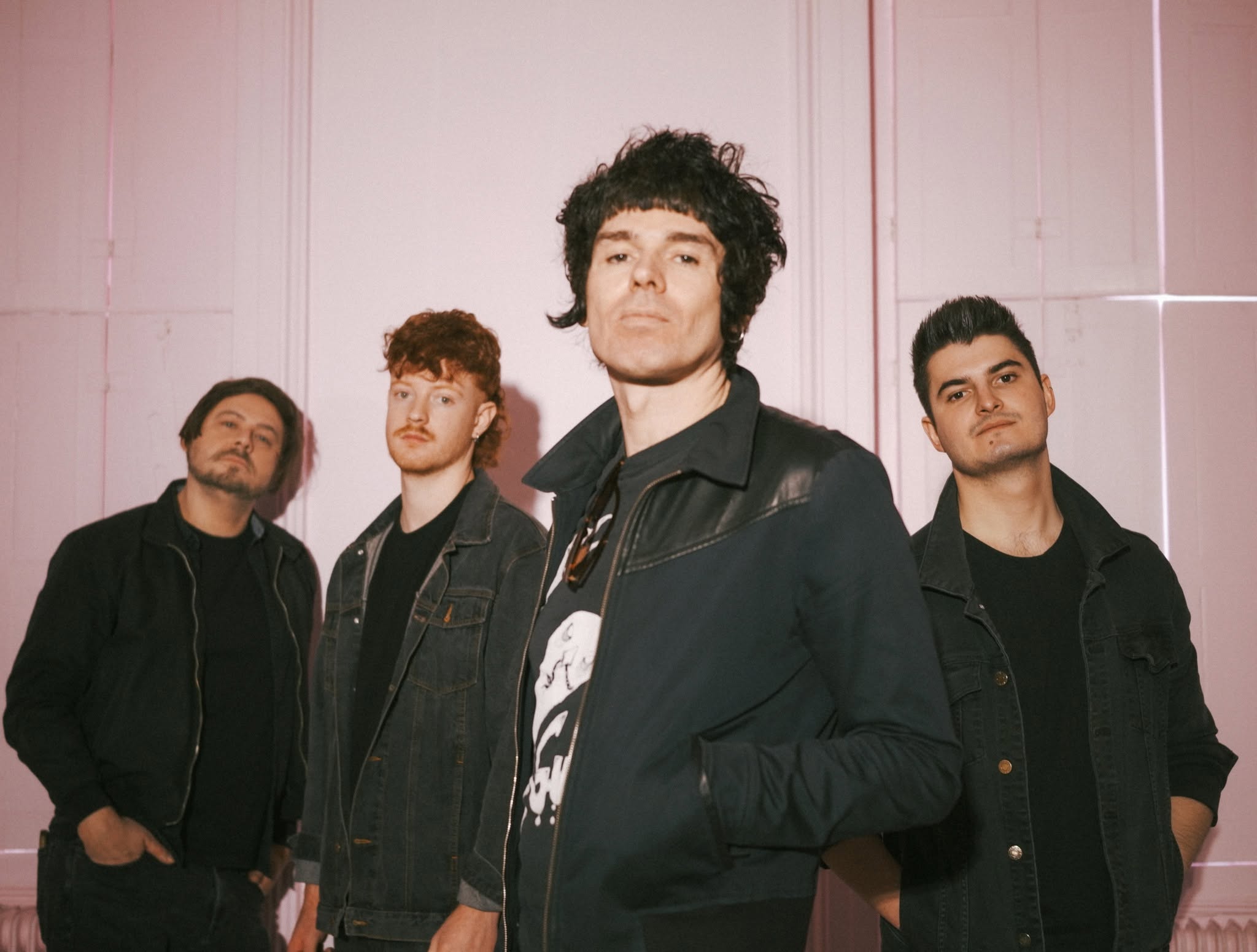 Four young men in dark jackets pose against a pink wall for The Unsigned Guide Spotlight: October 2026
